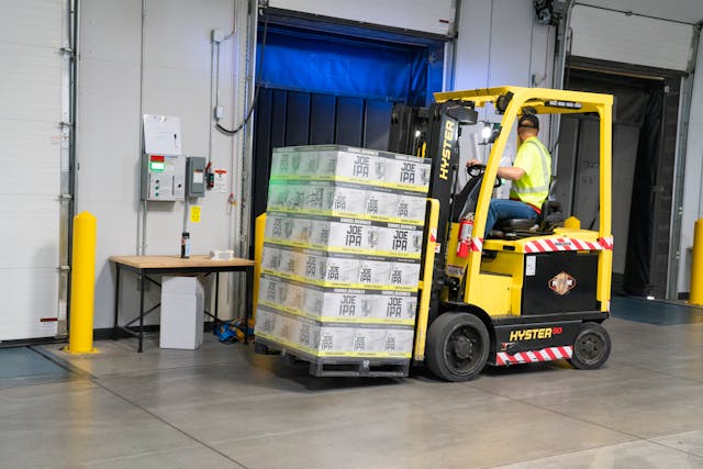 Forklift operator moving a loaded pallet inside a warehouse